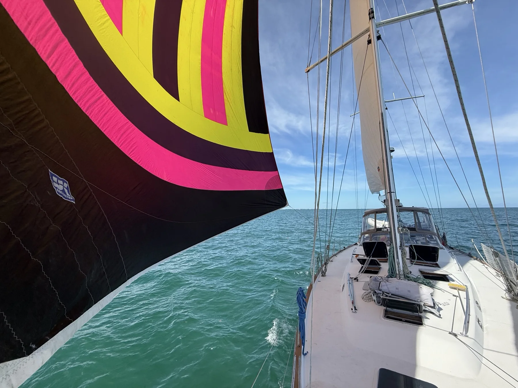 Sailboat underway with a colorful spinnaker deployed over blue water